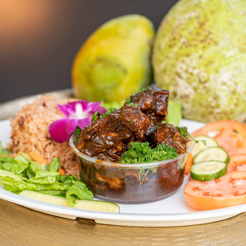 A Jamaican meal with brown stew chicken, rice and peas, salad, and a purple orchid.