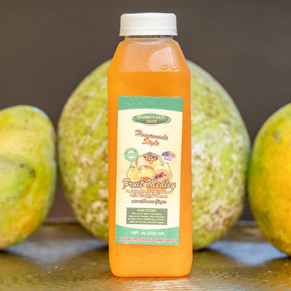 A bottle of Hazel's Island's Best Fruit Medley juice, with papayas and mangoes in the background.