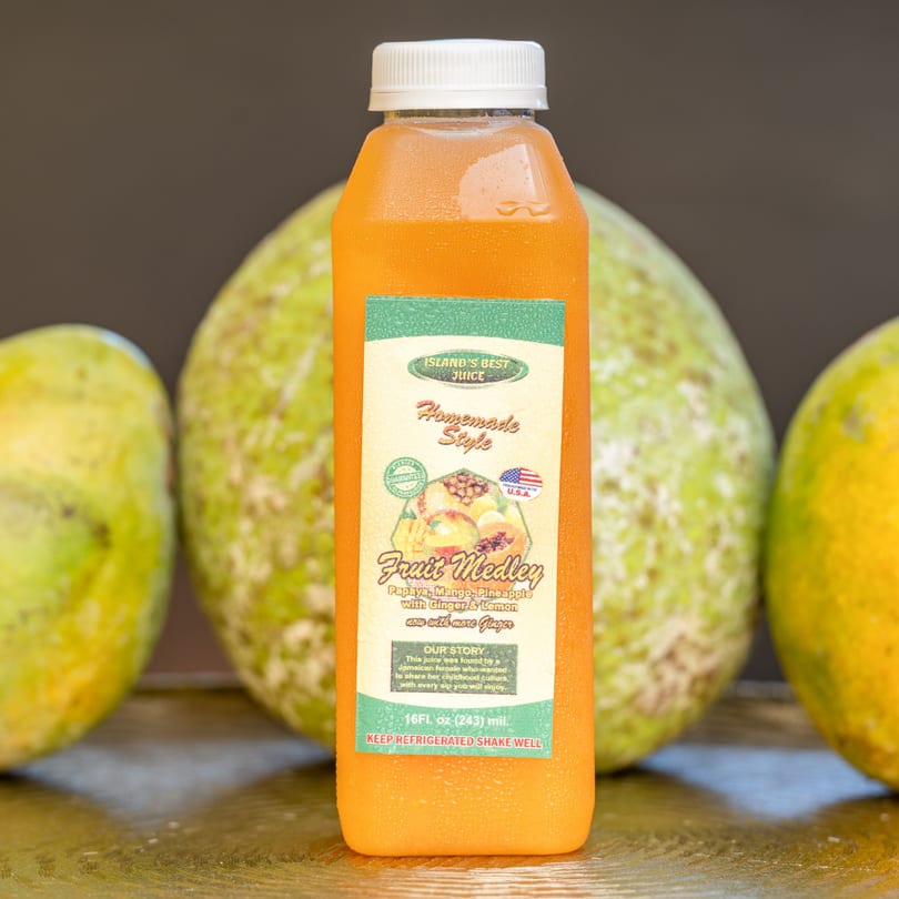 A bottle of Hazel's Island's Best Fruit Medley juice, with papayas and mangoes in the background.