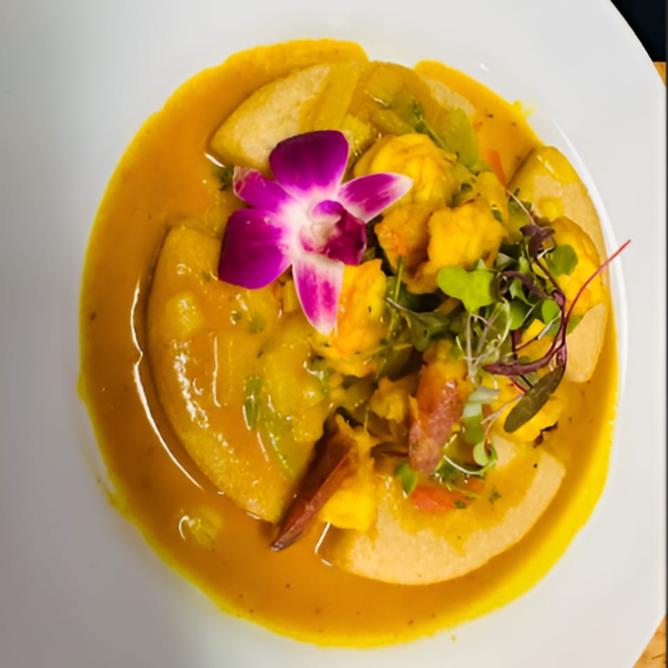Hazel's Jamaican curry dish with plantains, garnished with microgreens and a purple orchid.