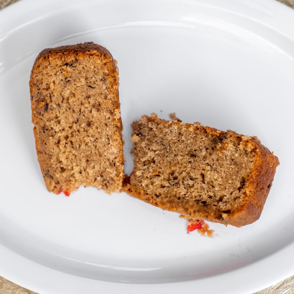 Two slices of Jamaican rum cake with red fruit pieces on a white plate.