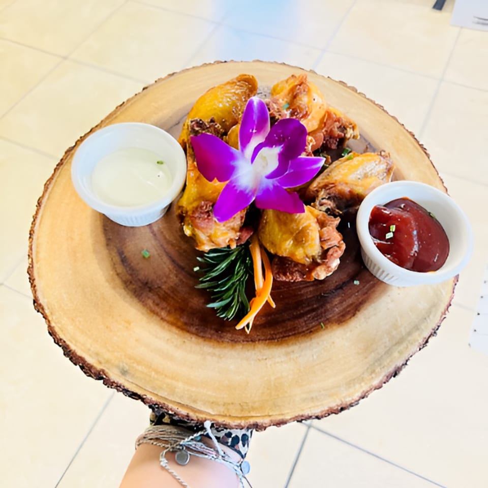 Hazel's Jamaican jerk chicken wings with dipping sauces, garnished with a purple orchid on a wooden platter.